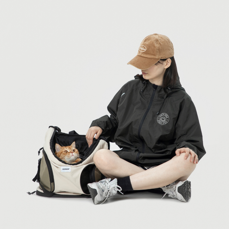 Cat in cream carrier backpack beside seated woman reading magazine