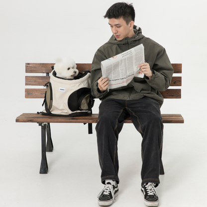 White cat in cream carrier backpack beside man reading newspaper
