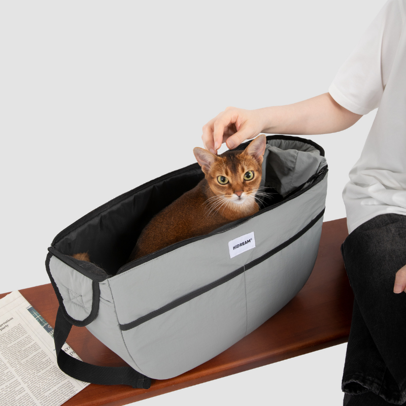 Owner petting cat inside gray outdoor pet tote shoulder bag on bench