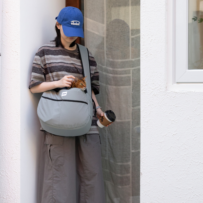 Owner standing with gray outdoor pet tote shoulder bag and drink