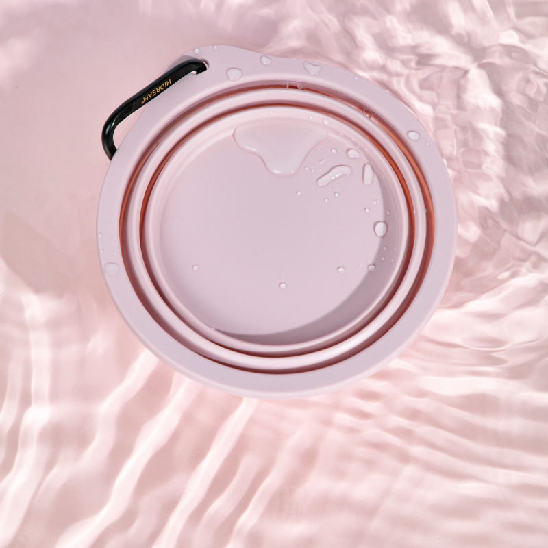 Pink collapsible travel pet bowl with water on fabric