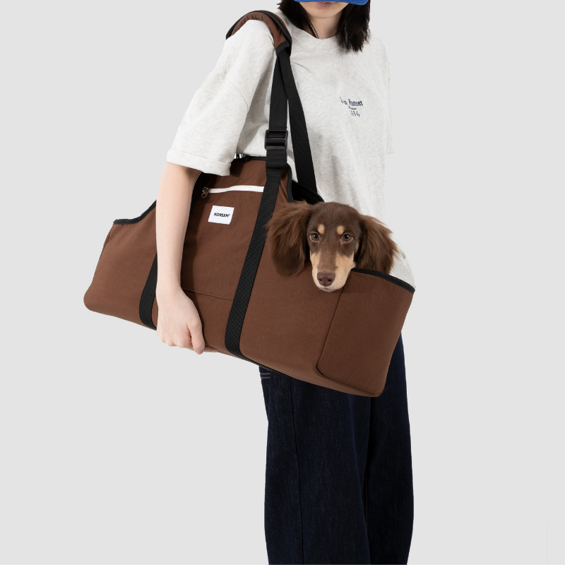 Owner wearing brown baguette-style pet shoulder carrier with dachshund inside