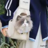 Fluffy gray and white cat with blue eyes peeking out of beige HAJIMI pet carrier sling bag