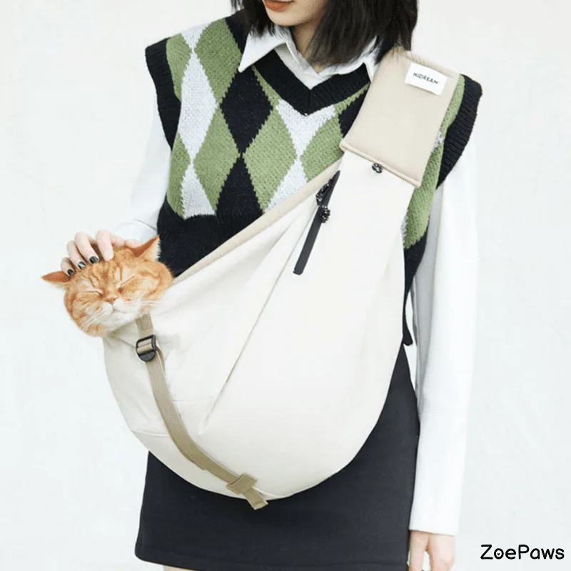 Woman wearing argyle sweater vest carrying orange cat in cream-colored ZoePaws pet sling carrier bag